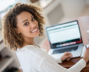 Young woman studying at home on a laptop and looking at the camera smiling