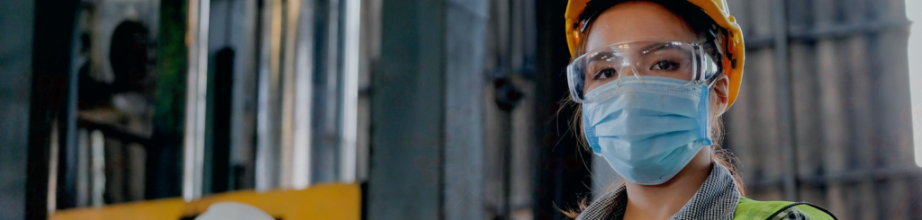 Close-up photo of young worker in factory wearing medical mask and safety glasses